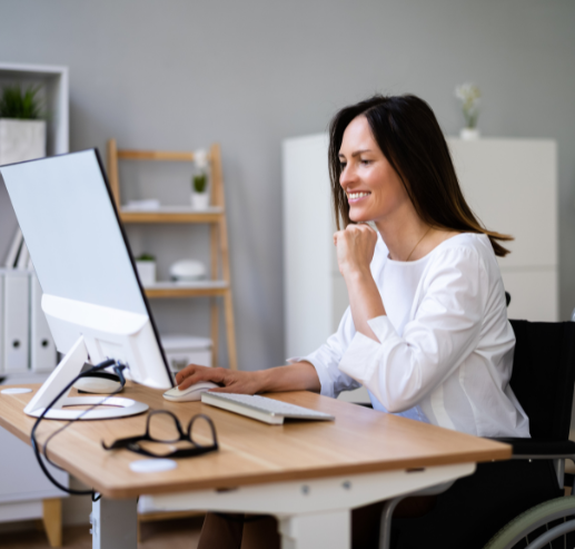 Smiling woman in wheelchair working on a desktop computer in modern office.